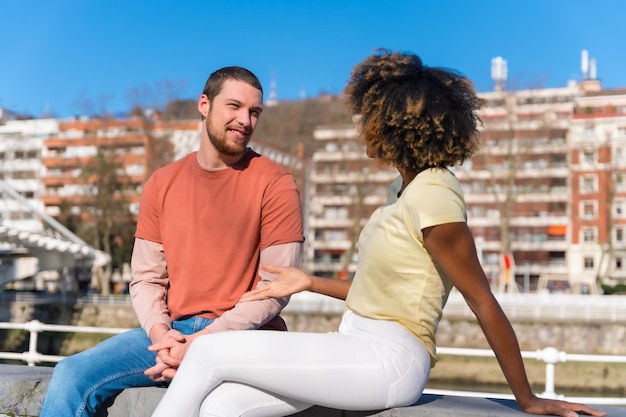 Coppia multirazziale sullo stile di vita della strada della città seduta sorridente parlando durante il fine settimana