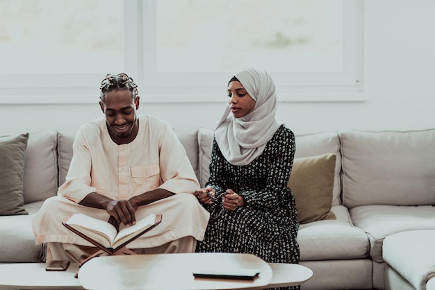 Coppia musulmana africana a casa durante il Ramadan che legge il libro sull'Islam dell'agrifoglio del Corano. Foto di alta qualità