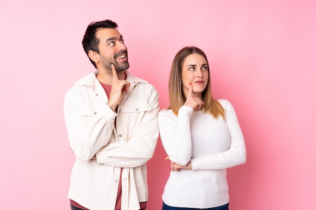 Coppia nel giorno di S. Valentino sopra la parete rosa isolata che pensa un'idea mentre guardano su