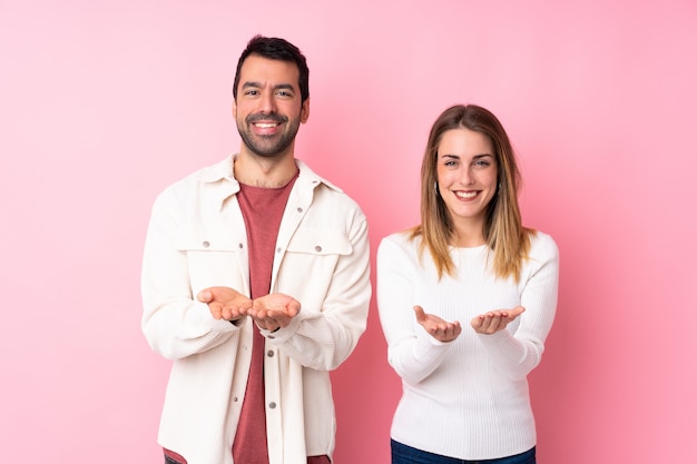 Coppia nel giorno di San Valentino sopra isolato muro rosa tenendo copyspace immaginario sul palmo per inserire un annuncio