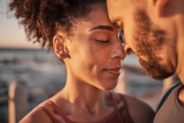 Coppia nera abbraccio e toccando la fronte abbracciando la relazione compassione o amore e cura sulla spiaggia Uomo e donna felici con le teste insieme sorridenti nella felicità per sostenere la fiducia o il romanticismo