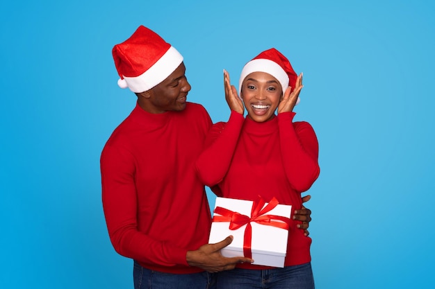 Coppia nera in cappelli di Babbo Natale che danno il presente sfondo blu di Natale