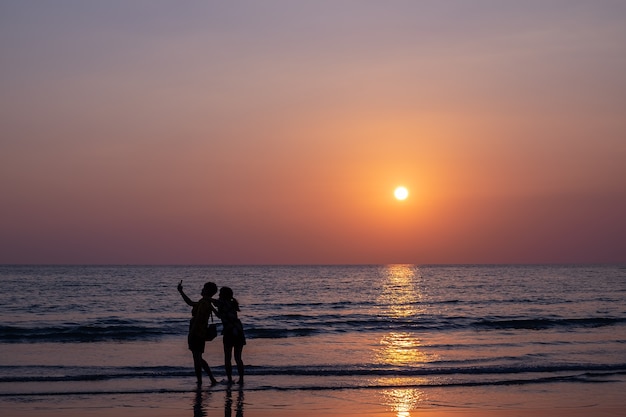 coppia prendendo selfie durante il tramonto sulla spiaggia