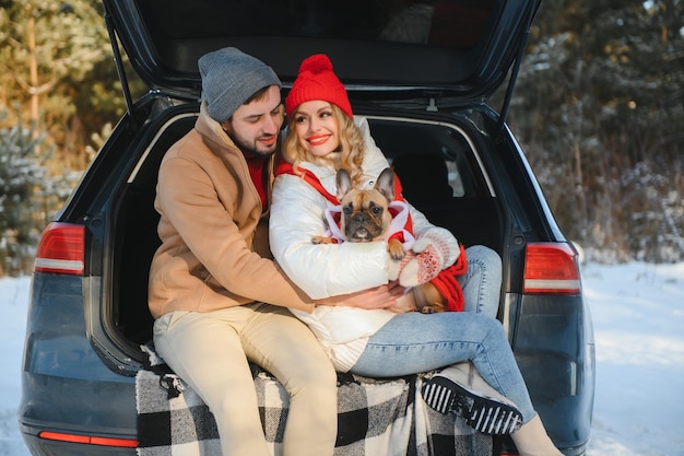 Coppia ragazzo e ragazza seduti in macchina che giocano con il cane nella foresta invernale