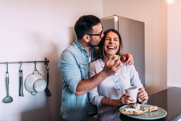 Coppia ridere mentre si mangia la colazione in cucina.