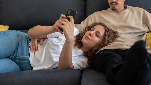 Coppia rilassante sul divano nell'accogliente appartamento Donna che trascorre del tempo al telefono mentre il ragazzo guarda la TV Tecnologia e concetto di dipendenza da Internet