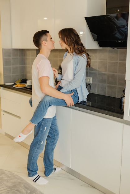 Coppia romantica a casa. La giovane donna attraente e l'uomo bello stanno godendo trascorrendo del tempo insieme in cucina moderna leggera. Concetto di relazione.