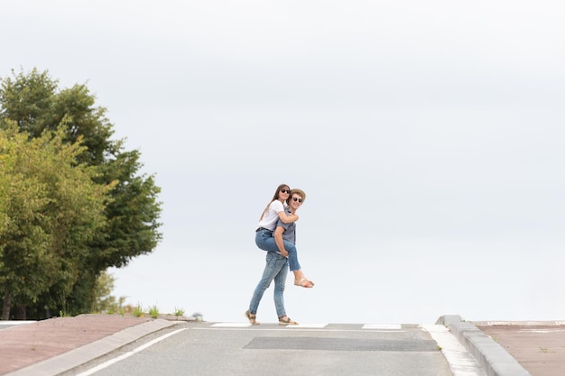 Coppia romantica che attraversa la strada. Giovane che porta sulla schiena o fidanzata sulle spalle. Composizione minima con spazio di copia.