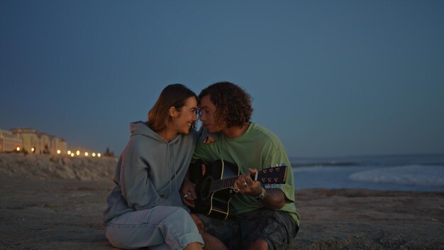 Coppia romantica che si diverte con la musica della chitarra serata natura del mare uomo riccio che suona una canzone