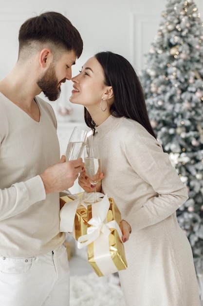 Coppia romantica in piedi vicino all'albero di Natale con bicchieri di champagne