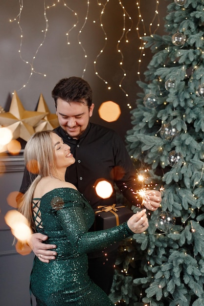 Coppia romantica in piedi vicino all'albero di Natale in possesso di stelle filanti