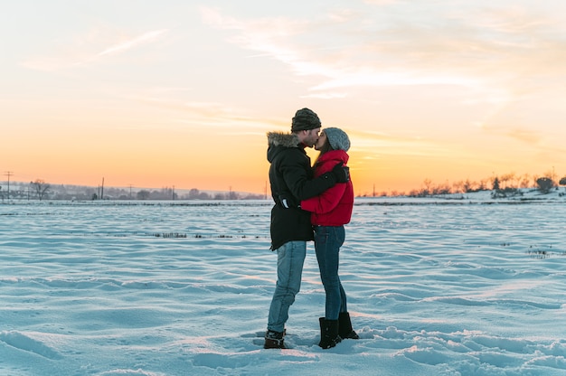 coppia romantica innamorata che indossa vestiti caldi che abbracciano e si baciano dolcemente nella campagna invernale innevata