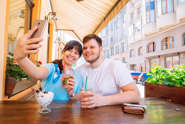 Coppia seduta al caffè in un giorno d'estate prendendo selfie bevande fresche