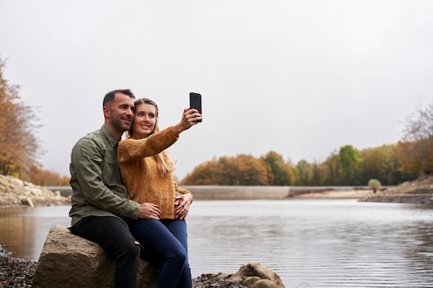 Coppia seduta davanti al lago facendo un selfie all'aperto con un lago