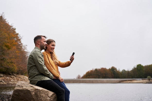 Coppia seduta davanti al lago facendo un selfie