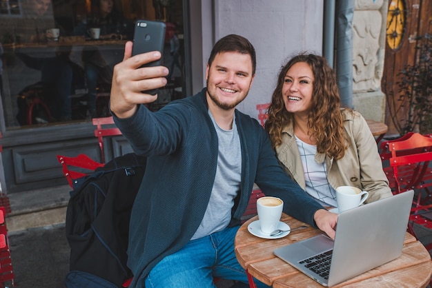 Coppia seduta in un caffè uomo che lavora al computer portatile donna che scatta foto sul telefono