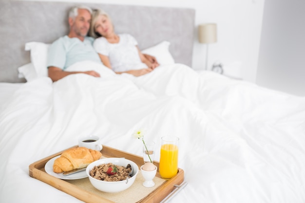 Coppia seduta sul letto con colazione in primo piano