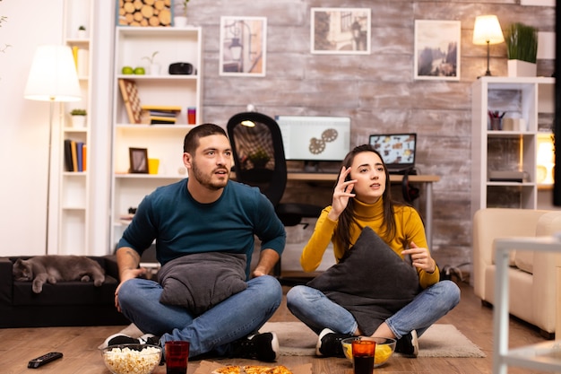 Coppia seduta sul pavimento e guardare la TV nel loro soggiorno.