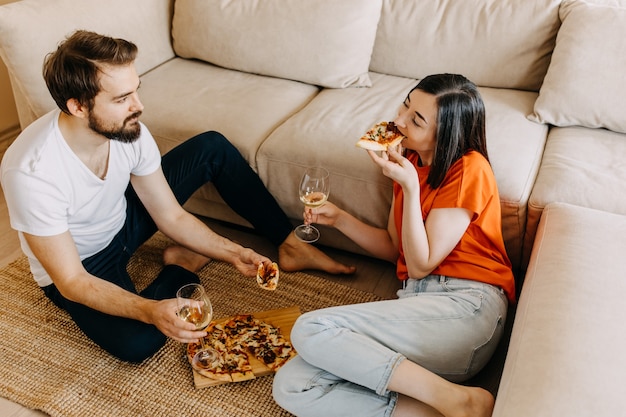 Coppia seduta sul pavimento, mangiare pizza e bere vino