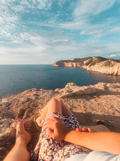 Coppia seduta sulla scogliera godendo della vista del tramonto sul mare