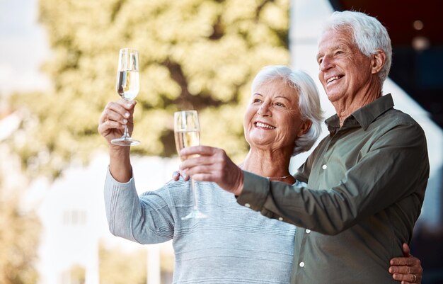 Coppia senior brindisi con champagne e abbraccio con relazione d'amore felicità e cura nel cortile di casa Uomo anziano donna e bicchiere per celebrare il romanticismo o l'anniversario di matrimonio con il sorriso in estate