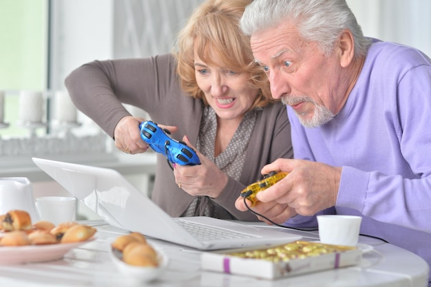 Coppia senior che gioca al computer con il laptop mentre beve t