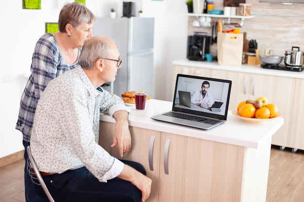 Coppia senior che ha una videoconferenza con un medico che parla di maltrattamenti utilizzando la webcam del laptop. Consultazione sanitaria online per anziani farmaci consulenza malattia sui sintomi, web di telemedicina medico