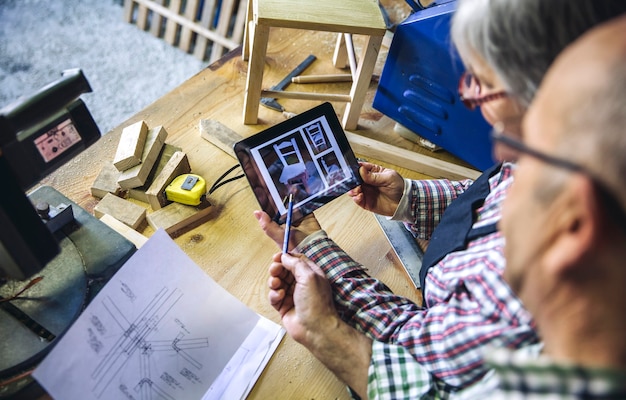 Coppia senior che lavora in un laboratorio di falegnameria cercando tablet con design sedia