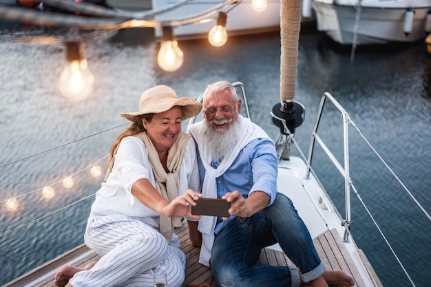 Coppia senior che si diverte a fare selfie in barca a vela durante le vacanze estive - Focus principale sulla faccia dell'uomo anziano