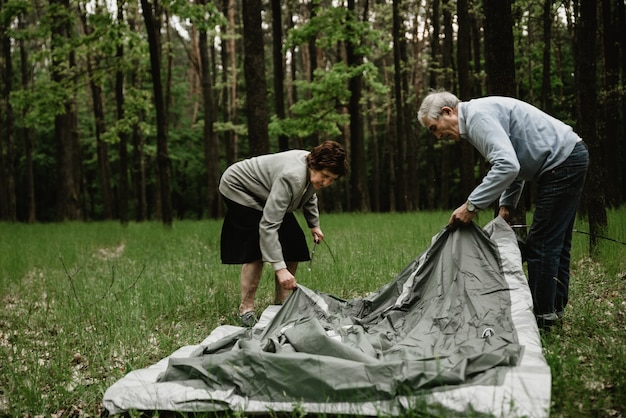 Coppia senior godendo le vacanze e sta installando la tenda. Adulti che trascorrono le vacanze estive nella natura e montano una tenda. Seniors è campeggio e montaggio tenda