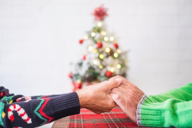 Coppia senior in abiti caldi che si tengono per mano davanti all'albero di Natale decorato a casa. Amare la vecchia coppia eterosessuale romantica che celebra insieme la festa di natale