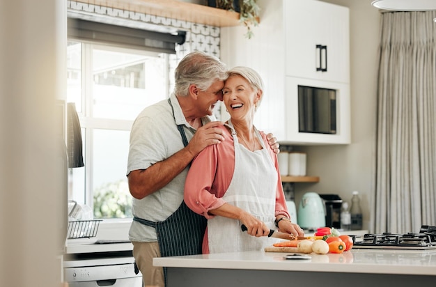 Coppia senior in cucina che cucina cibo sano insieme e felice nello stile di vita in pensione Donna anziana che taglia le verdure con il grembiule vecchio uomo bianco abbraccio moglie in casa e amore nutrizione cena pasto