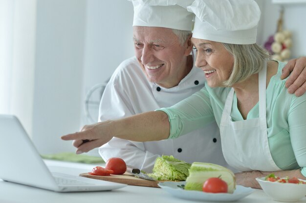 Coppia senior in cucina che cucina con il laptop