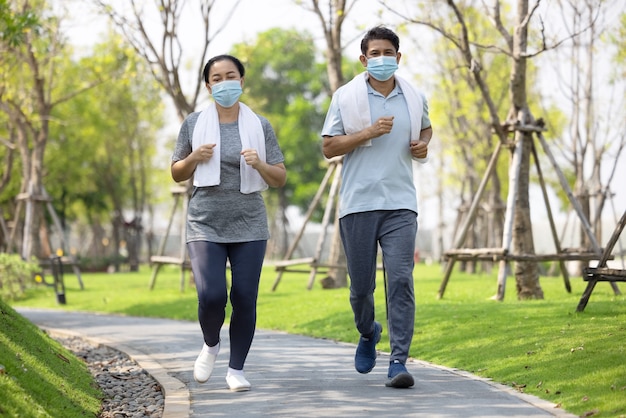 Coppia senior indossando la maschera per il viso e camminando attraverso il parco naturale, allenamento estivo all'aperto