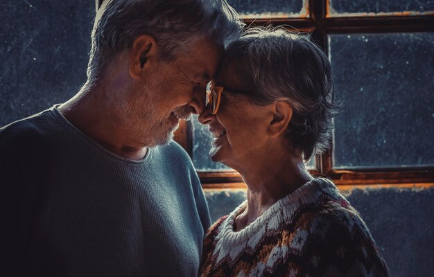 Coppia senior matura innamorata e romantica attività per il tempo libero a casa faccia a faccia toccando davanti e sorridendo in relazione Vacanze invernali Natale al coperto per uomo e donna vecchiaia in felicità