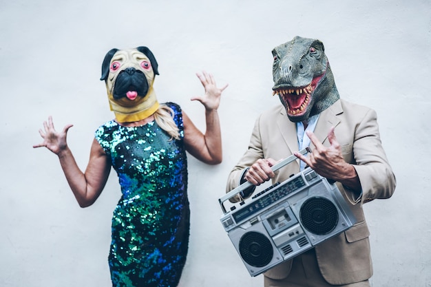 Coppia senior pazza che balla per la festa indossando t-rex e maschera di pollo - Vecchi alla moda che si divertono ad ascoltare musica con stereo stereo