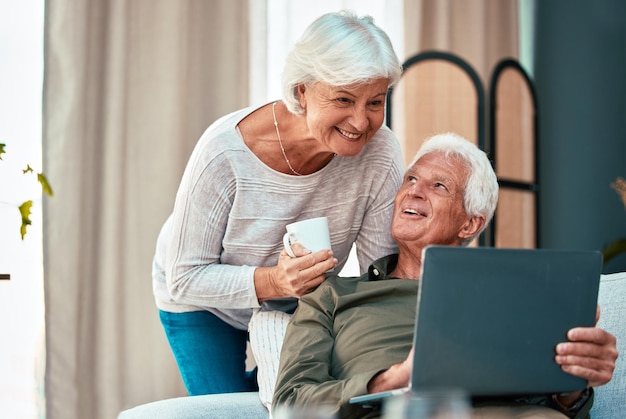 Coppia senior portatile e felice a casa sul divano lounge parlando e leggendo online per lo shopping online social media o risparmi sul sito web bancario Vecchio e donna insieme a caffè e wifi