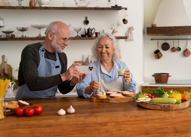 Coppia senior prendendo selfie durante la cottura insieme in cucina