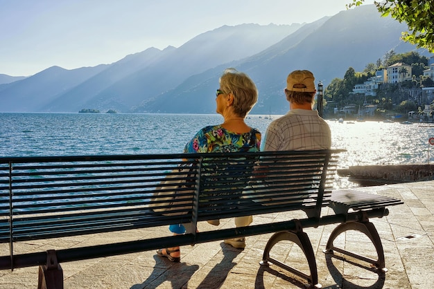 Coppia senior seduta sulla panchina presso l'argine di Ascona lussuoso resort sul Lago Maggiore, Canton Ticino in Svizzera.