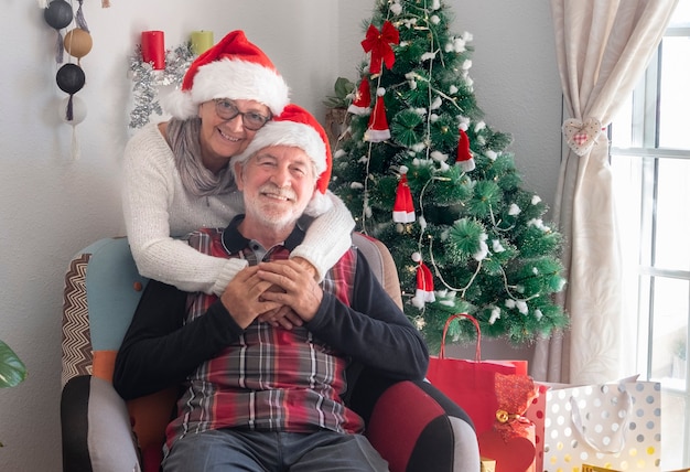 Coppia senior sorridente di due nonni con cappelli di Babbo Natale in attesa della famiglia - buon Natale a casa per due anziani pensionati che si godono le vacanze