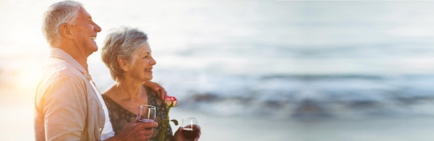 Coppia senior tenendo bicchieri di vino rosso e rosa in spiaggia