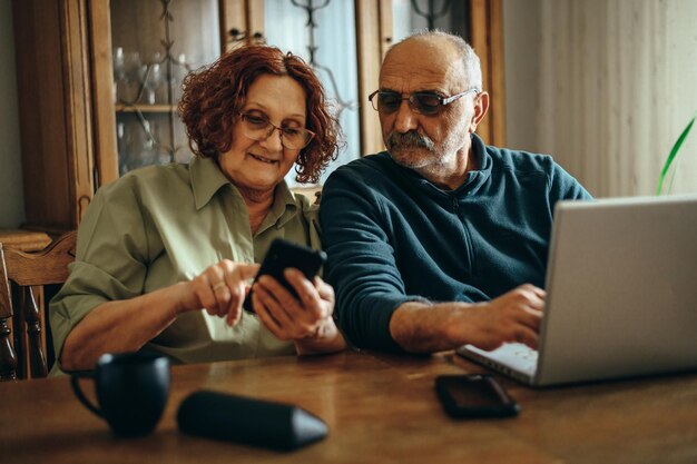 Coppia senior utilizzando uno smartphone e un laptop a casa