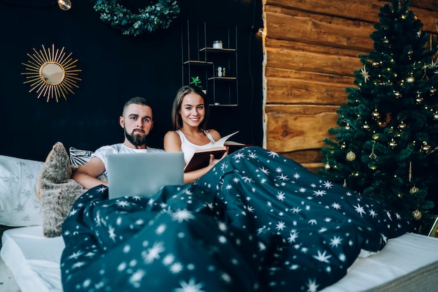 Coppia sorridente a letto con laptop e libro