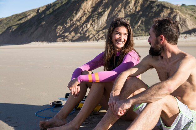 Coppia sorridente con tavola da surf seduto sulla spiaggia