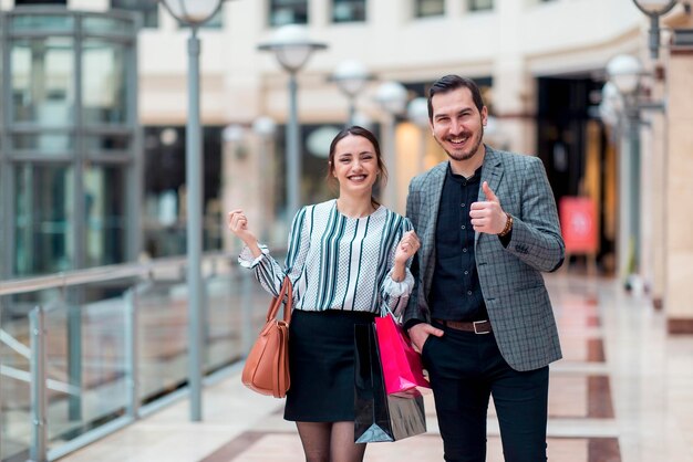 Coppia sorridente dall'aspetto moderno in un centro commerciale che stanno gesticolando segno giusto e sono felici