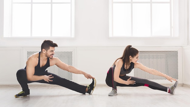 Coppia sportiva che allunga le gambe prima dell'allenamento in studio, panorama, spazio copia