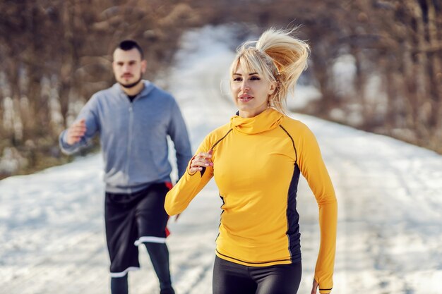 Coppia sportiva che corre nella foresta al giorno di inverno nevoso. Abitudini sane, maratona, fitness invernale