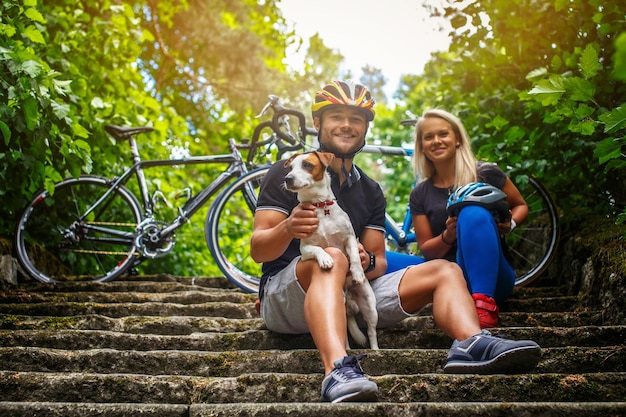 Coppia sportiva in posa con il loro cane dopo un giro in bicicletta in una foresta.