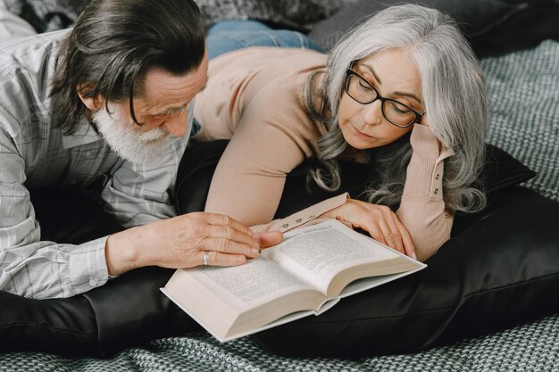 Coppia sposata invecchiata felice che si rilassa insieme a casa. Libro di lettura delle coppie senior sul letto.