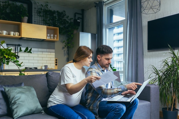 Coppia sposata marito e donna incinta che lavorano su scartoffie del computer portatile a casa